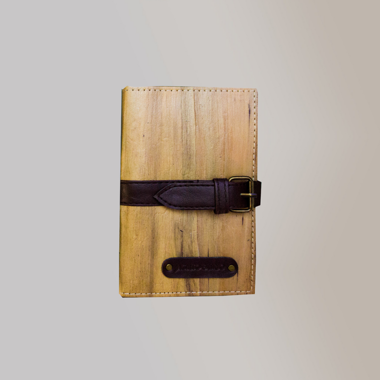 A journal with a vegan leather cover that gives it a wooden appearance and a black belt buckel closure.
