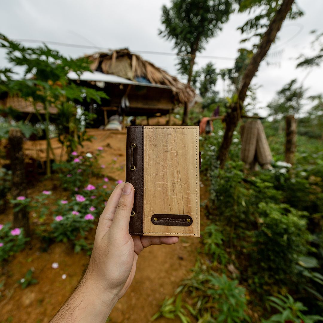 A small brown notebook with a leather bound spine being held up in front of a rural farm background.