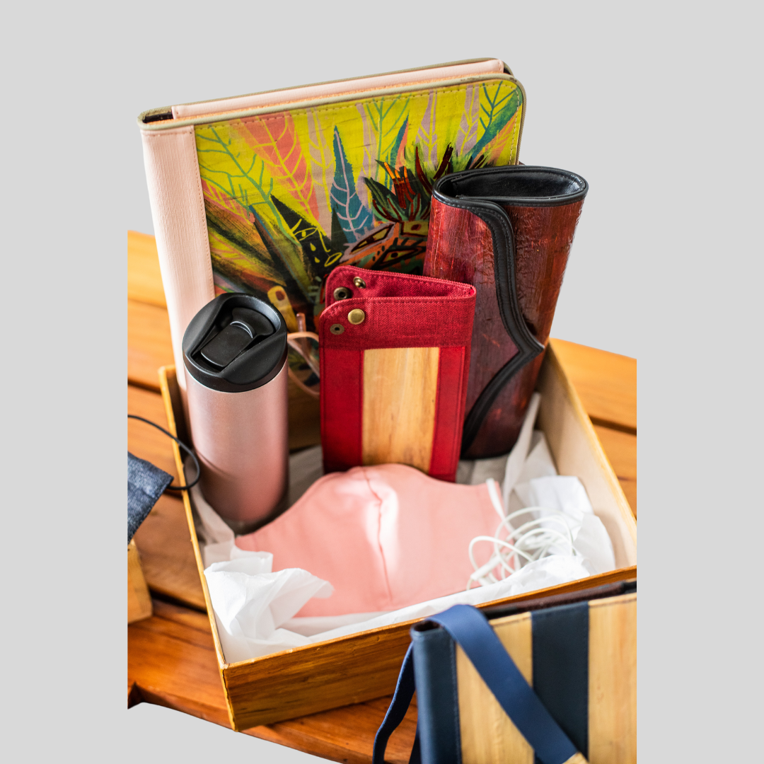 A gift set of products inside a wooden box, some of the products being a vegan leather clutch, a pink tumbler, a pink cloth mask, and more.