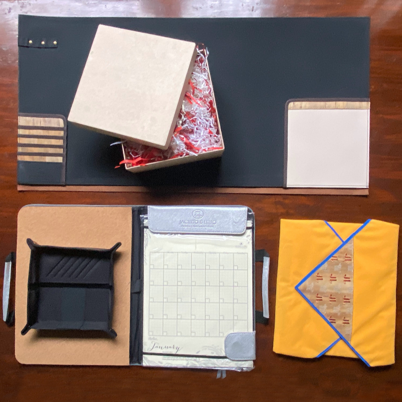 A bundle of vegan leather items perfect for an office employee, such as a deskmat with inlaid pockets, a wrappable laptop case, a catchall tray, and a planner with a corkboard.