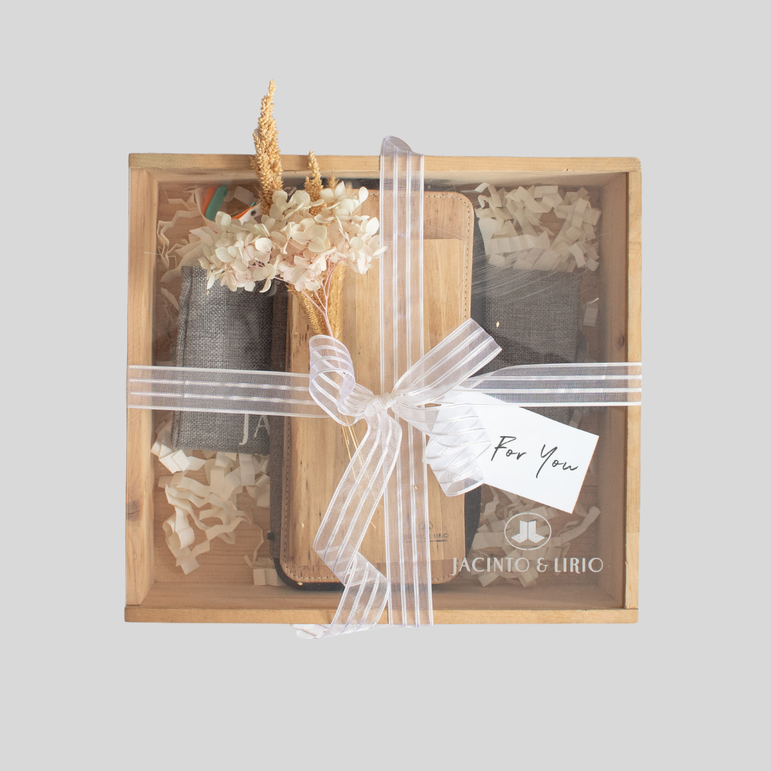 A wooden box containing vegan leather goods and wrapped with semi-transparent tulle fabric, tied together with a white ribbon.