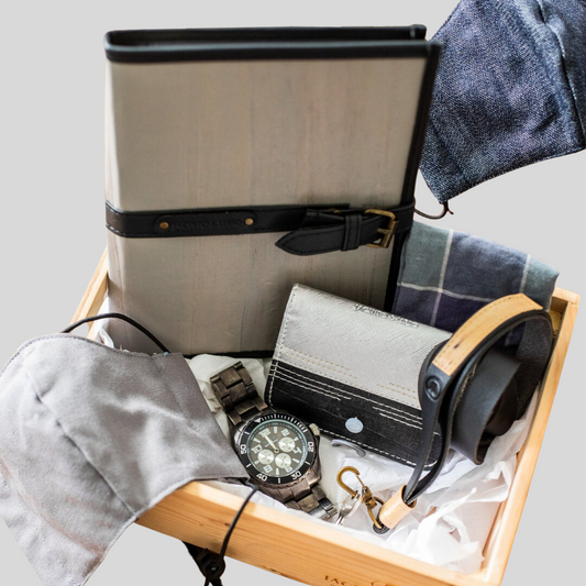A father's day gift set inside of a wooden crate, comprised of a gray vegan leather journal, a two-toned card wallet, a masculine watch, a gray cloth face mask, and an ID lanyard.