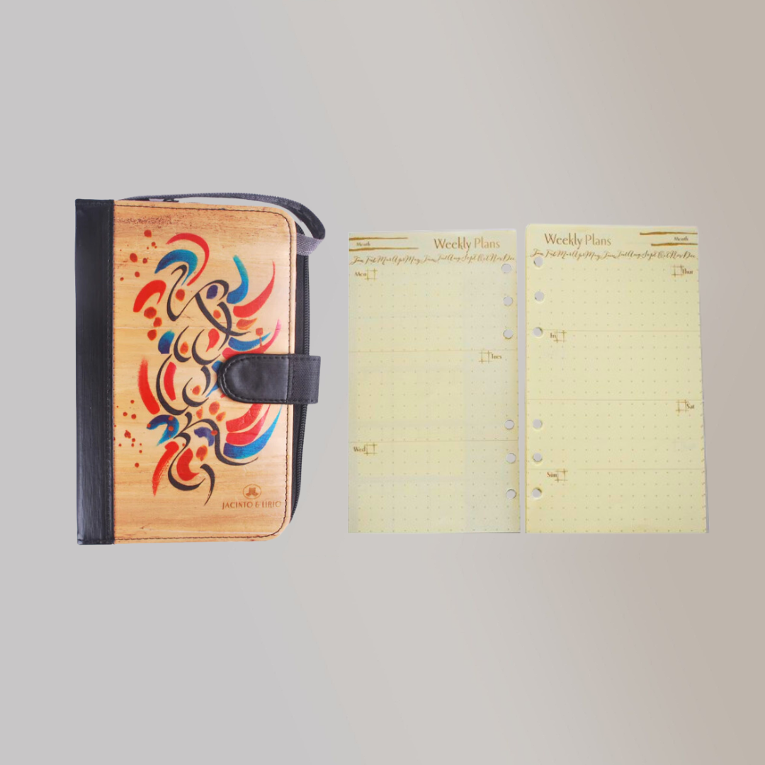An A6 vegan leather binder with blue, black, and red designs on its cover beside two blank extra refills for the pages.