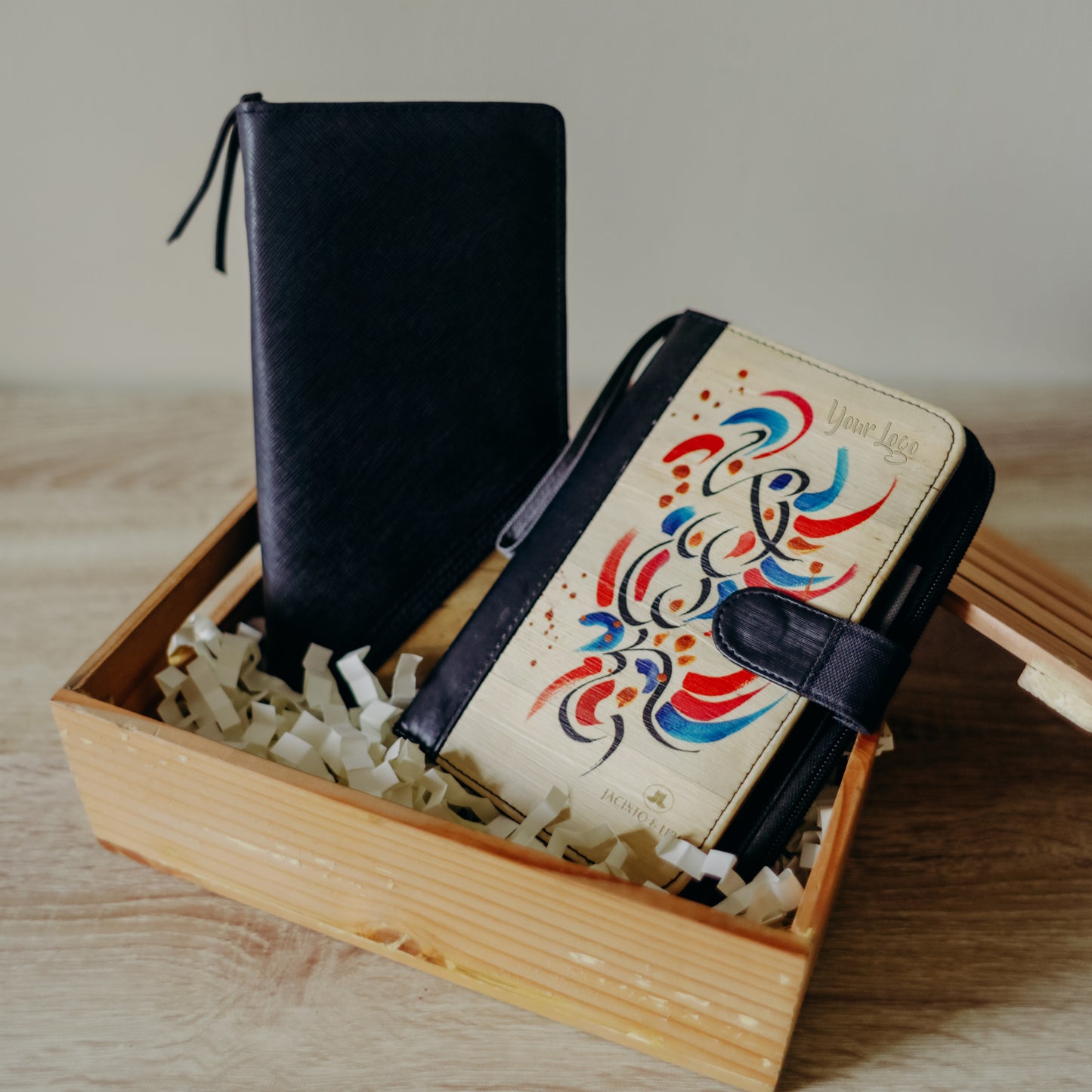 A vegan leather notebook with a vibrant painted blue and red design on its cover, laying inside of a wooden gift box.