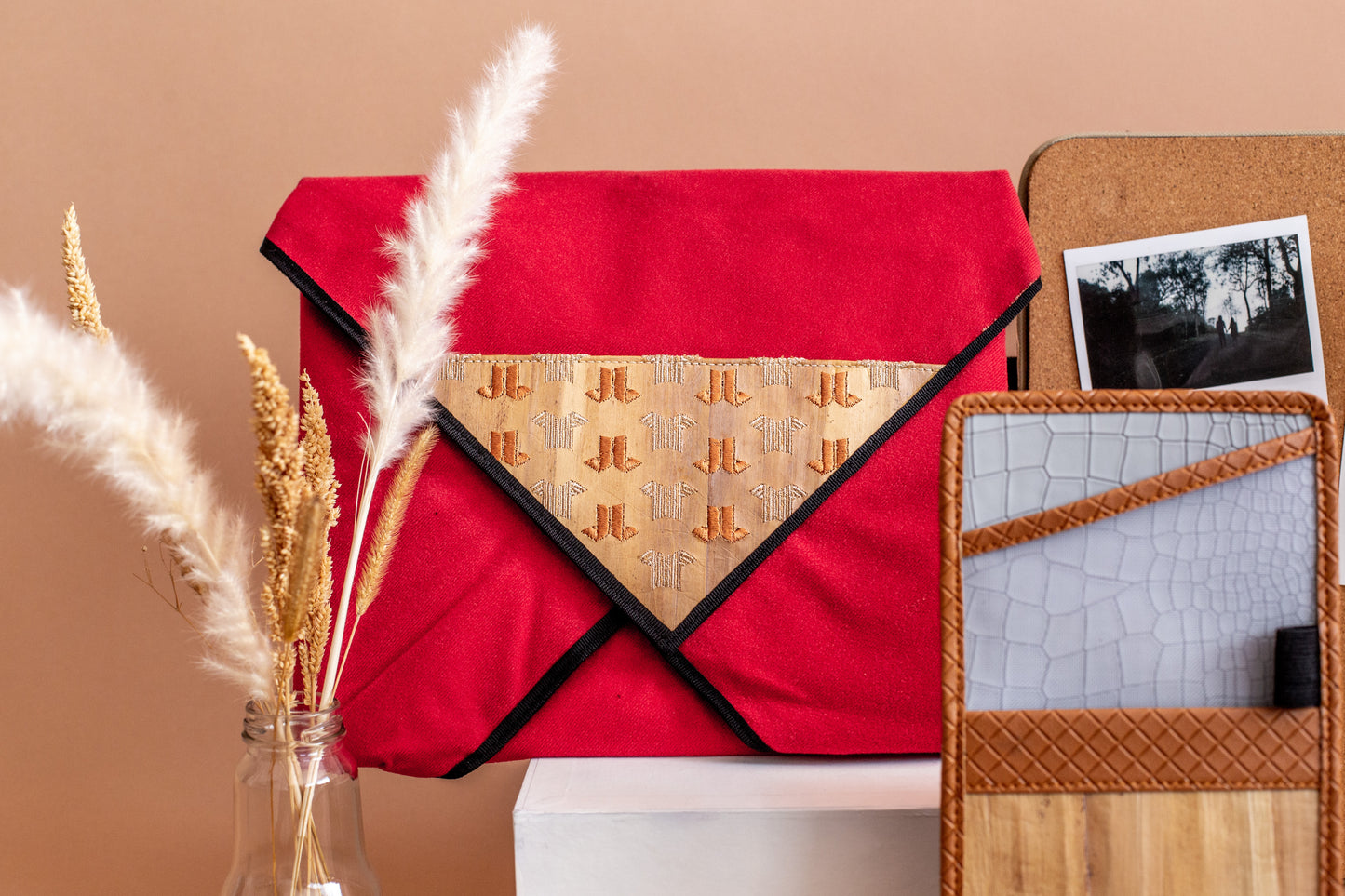 A bold red resizable wrap case for laptops made out of vegan leather, displayed on a shelf next to other vegan leather products.
