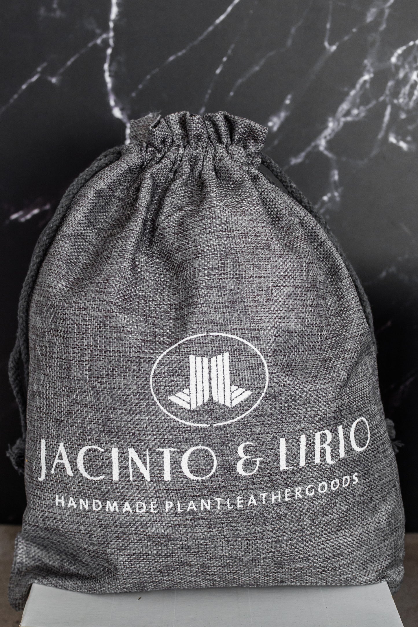 A gray drawstring bag with the Jacinto & Lirio logo on it in white.