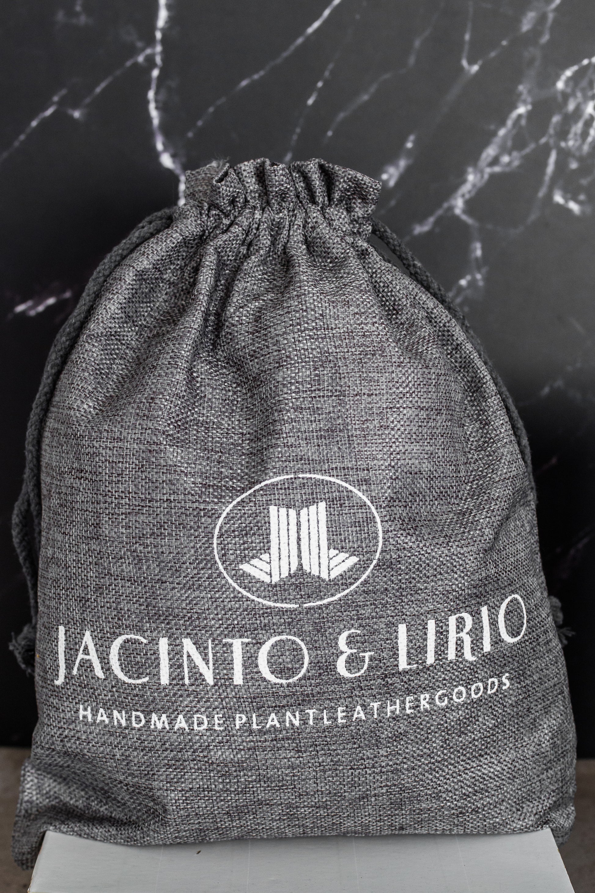 A gray drawstring bag with the Jacinto & Lirio logo on it in white.