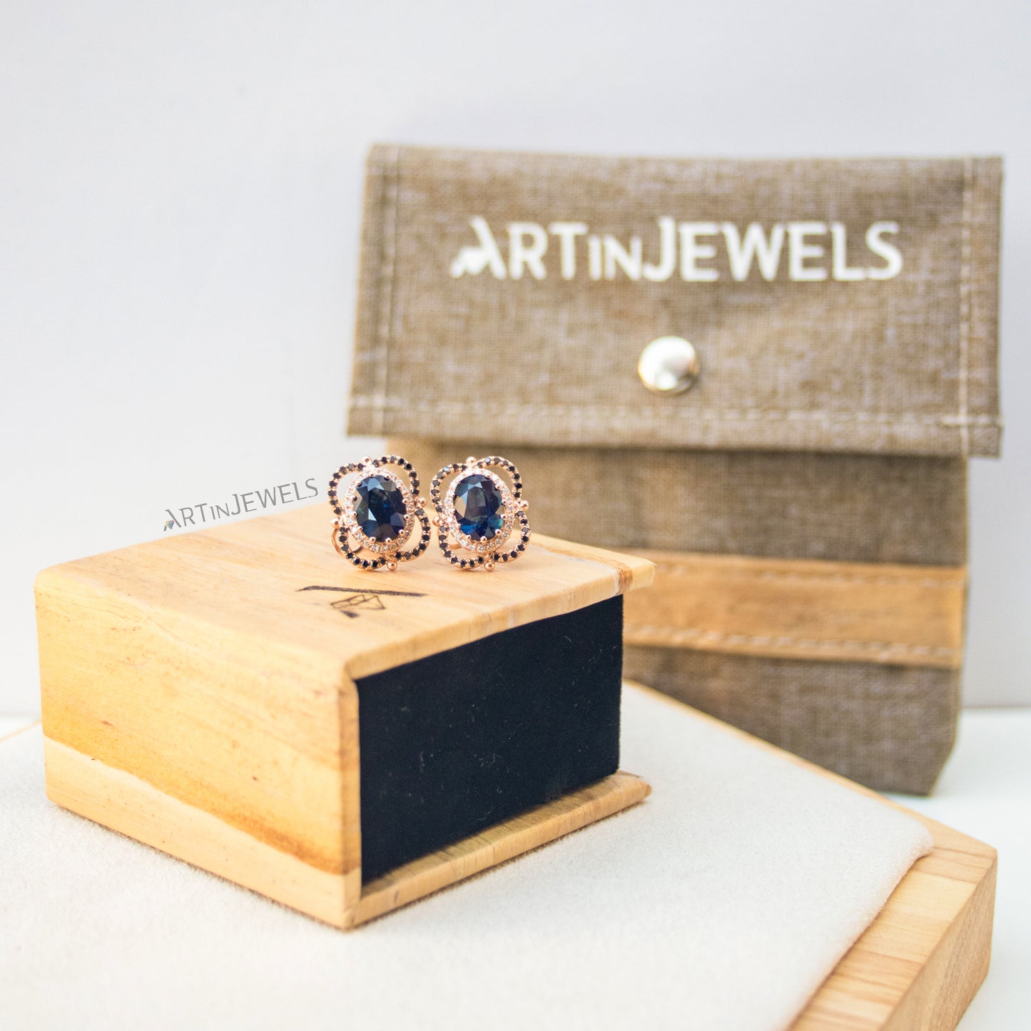 A jewelry box made of vegan leather with a wood-looking exterior, with a pair of blue gemstone earrings perched on top of the box and a brown purse in the background.