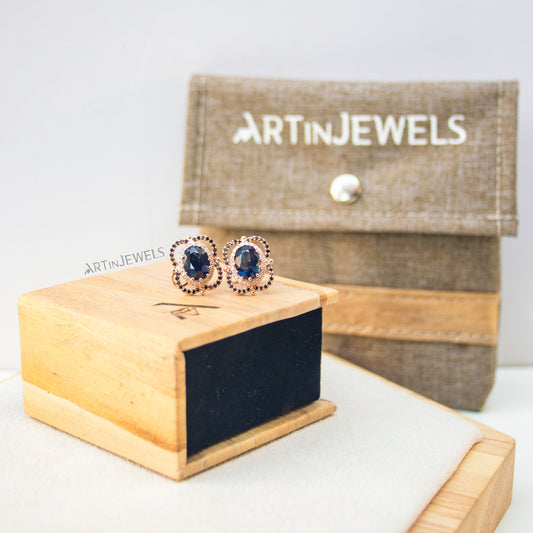 A jewelry box made of vegan leather with a wood-looking exterior, with a pair of blue gemstone earrings perched on top of the box and a brown purse in the background.