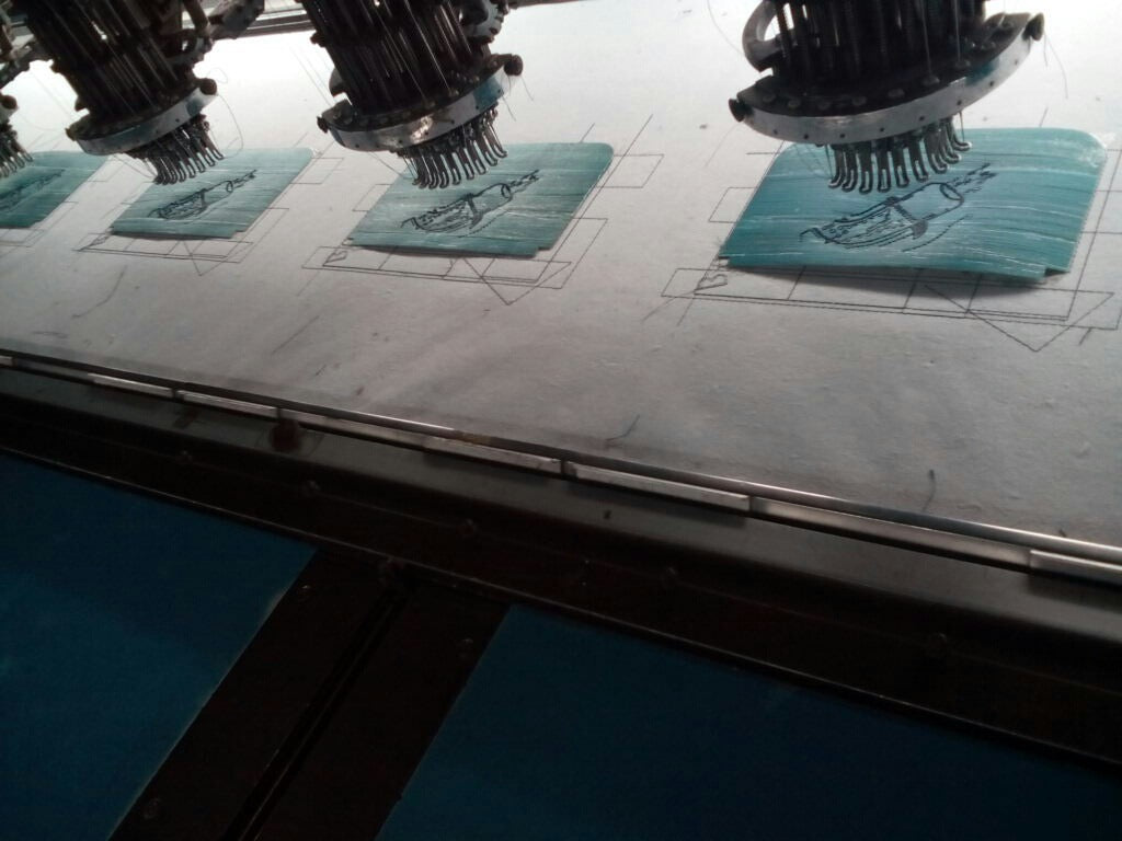 A lineup of cyan-colored vegan leather pieces being embroidered on by embroidery machines.