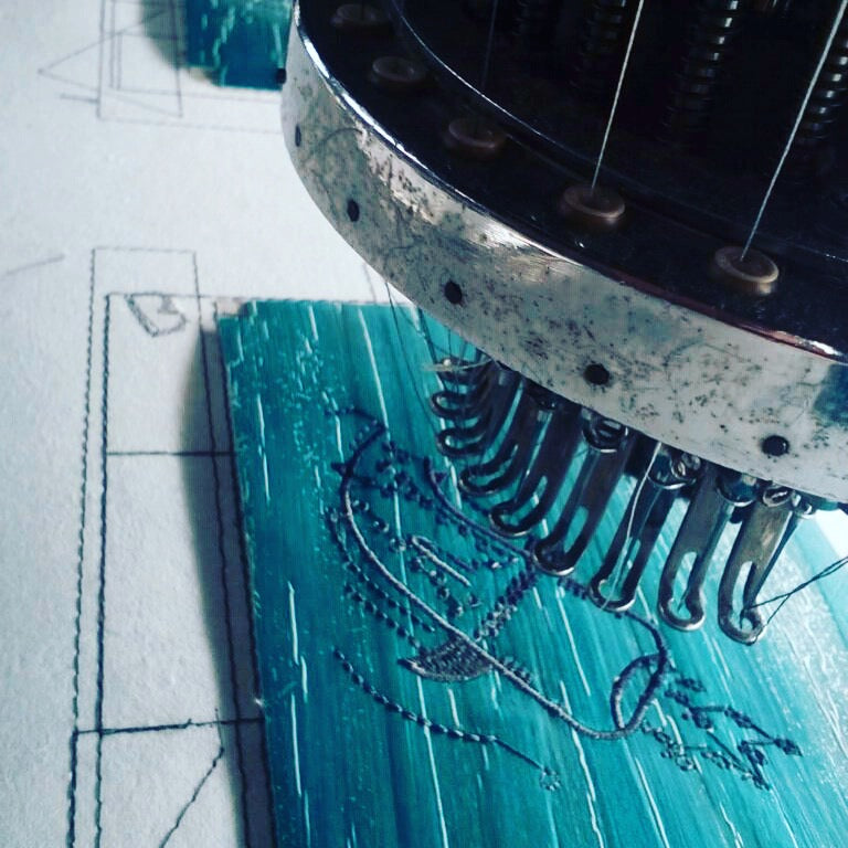 A cute illustration of a whale shark being embroidered on a piece of teal-dyed vegan leather using an embroidery machine.