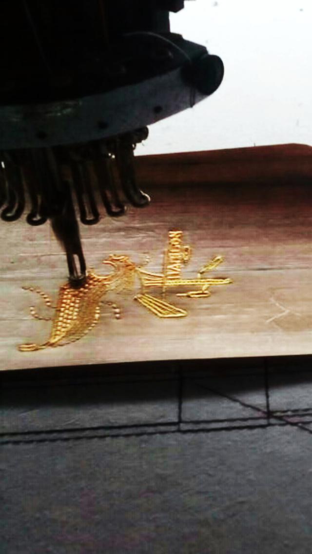 An intricate image being embroidered in gold thread on a skin of vegan leather, via an embroidery machine.