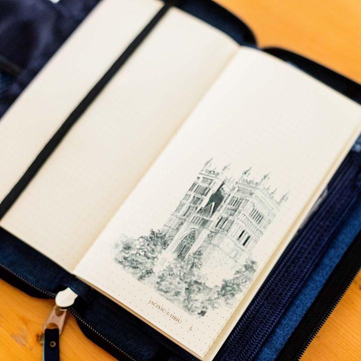 A blue vegan leather notebook that has an excellent pencil sketch of a medieval castle on one of the opened pages.