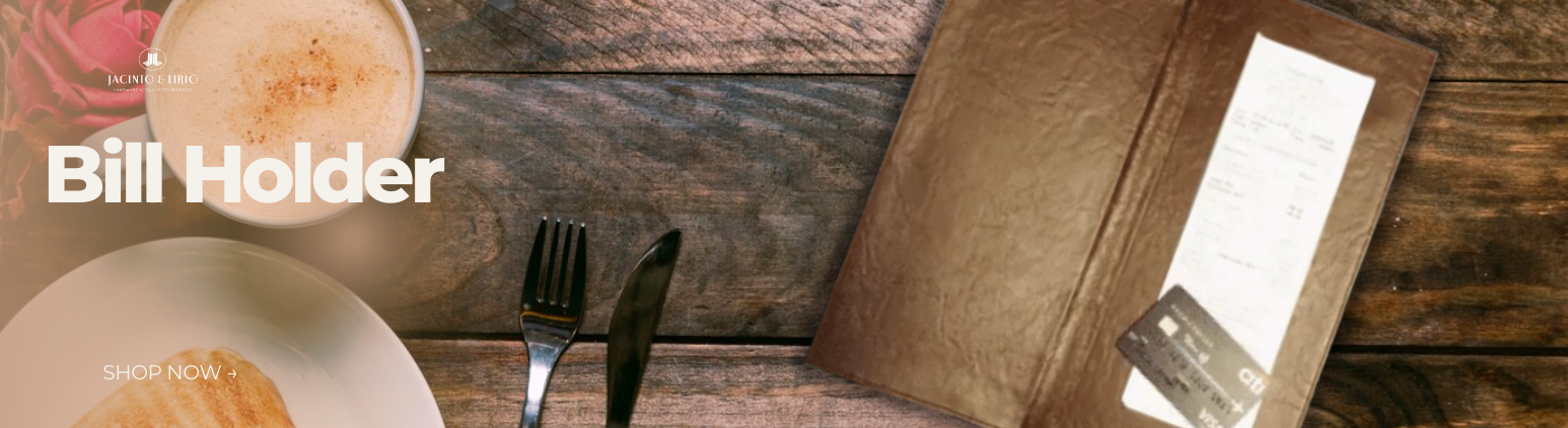 A restaurant table with a rustic wooden texture holds a cup of frothy coffee, a plate with a pastry, and a fork and knife on a napkin. To the right, there is a brown vegan leather bill holder containing a receipt and a credit card.