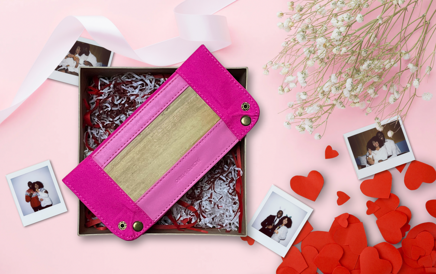 A barbie pink vegan leather foldable valet tray on top of an opened gift box on a pink table with some paper hearts and polaroids of a couple.