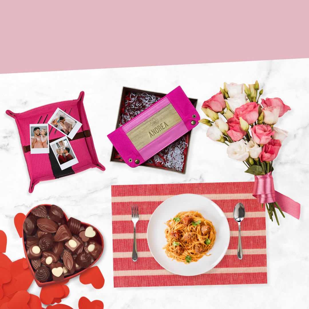 A pink place setting for a valentines day meal with spaghetti, a box of cholocates, a bouqet, a pink vegan leather wallet with the name "Andrea" engraved, and a hot pink vegan leather tray.