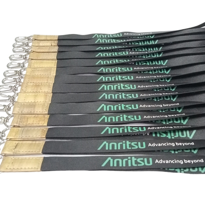 Multiple black Anritsu branded lanyards laid side-by-side, each featuring green "Anritsu Advancing Beyond" text, a light brown faux vegan leather accent, and a silver swivel clip. Ideal for corporate branding and event identification.