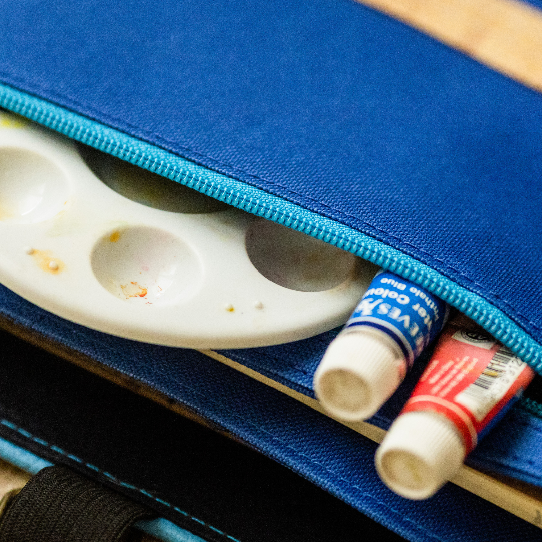 Some paint tubes and a paint pallet peeking out of a blue case.