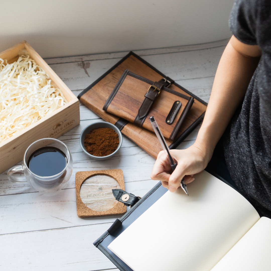 A person writing on a blank page of a black journal.