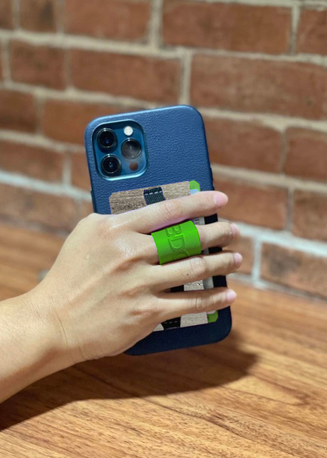 Close-up of a hand holding a phone with a multifunctional cellphone grip and card holder, featuring a green strap and vegan leather design.