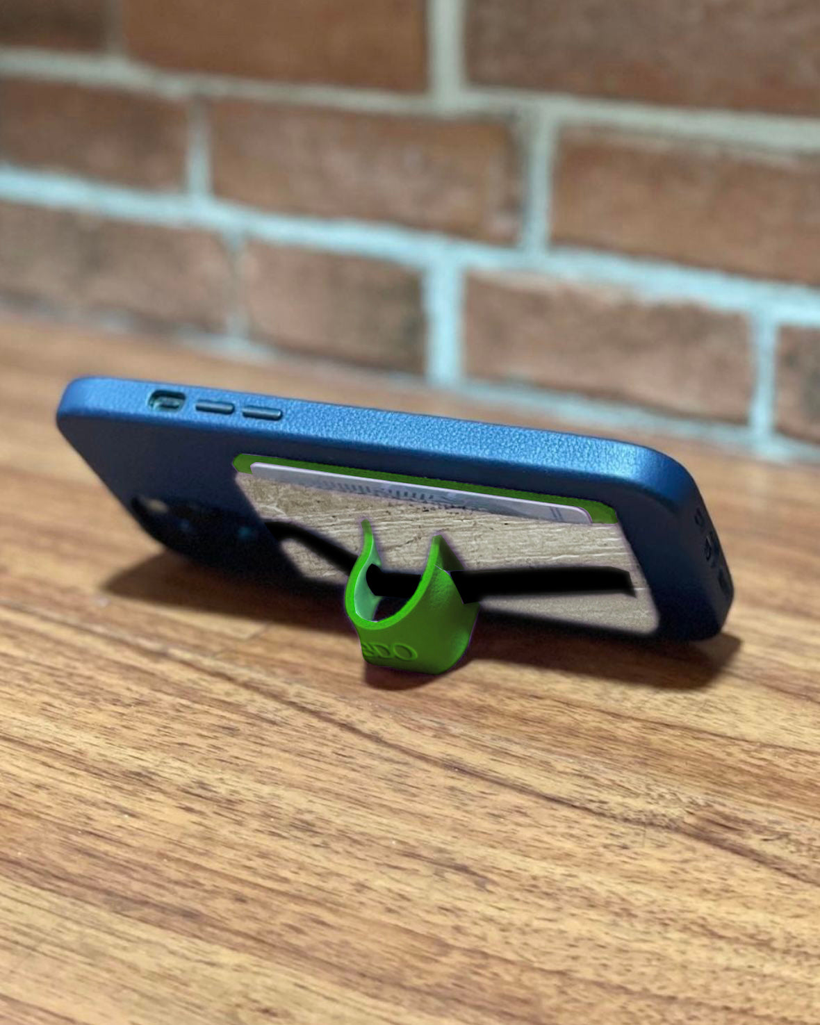 A multifunctional cellphone grip and card holder being used as a phone stand by folding the piece of green leather in on itself to create a shape.