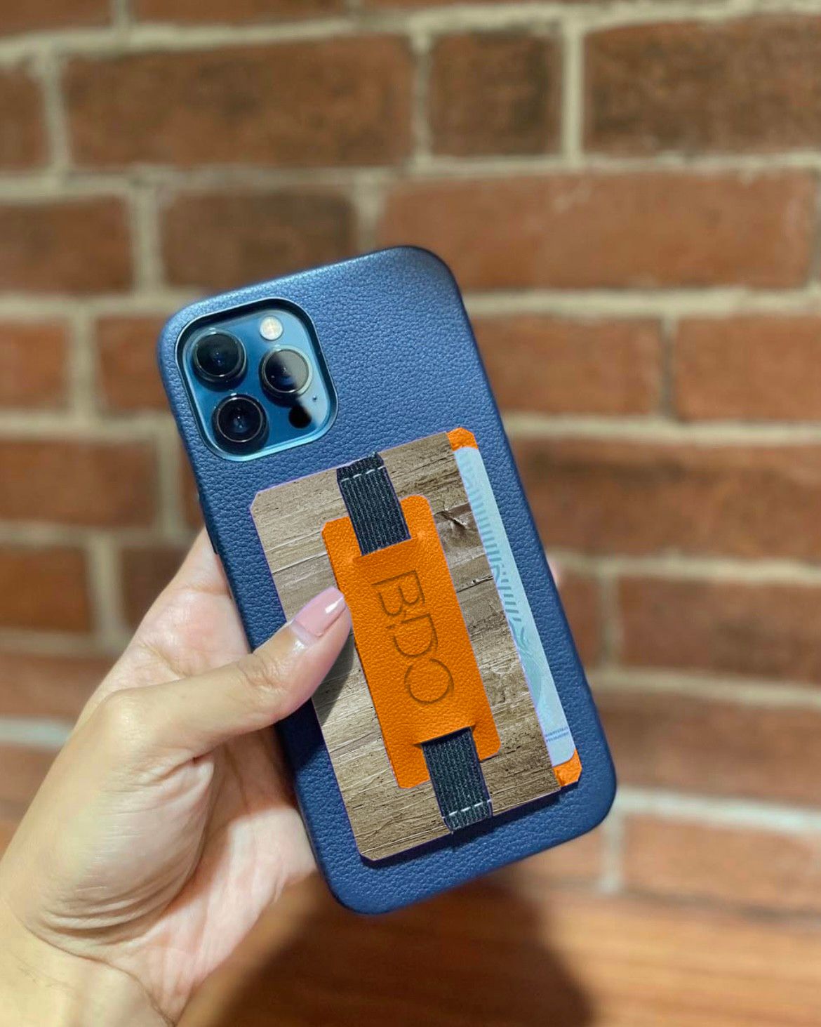 A blue iphone case adorned with a vegan leather multifunctional card holder and cellphone grip, with a orange leather accent.