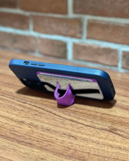 A cellphone stand made of purple vegan leather, that has its own hidden pocket for holding cards, attached to the back of a blue iphone.