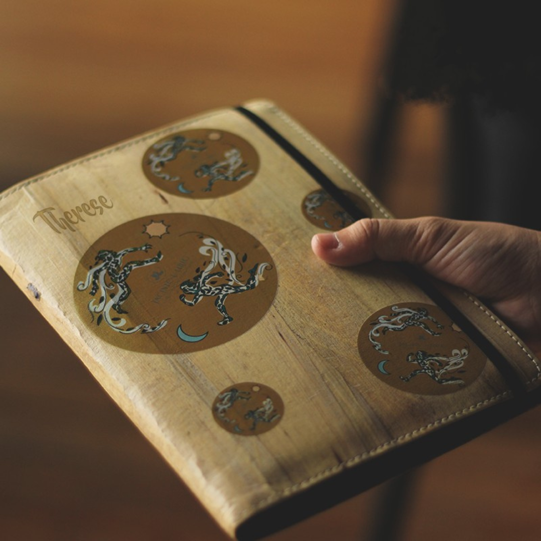 A hand holding a vegan leather journal with designs.