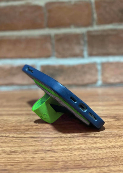 A side view of a green vegan leather cellphone grip being used as a phone stand by folding the leather in on itself.