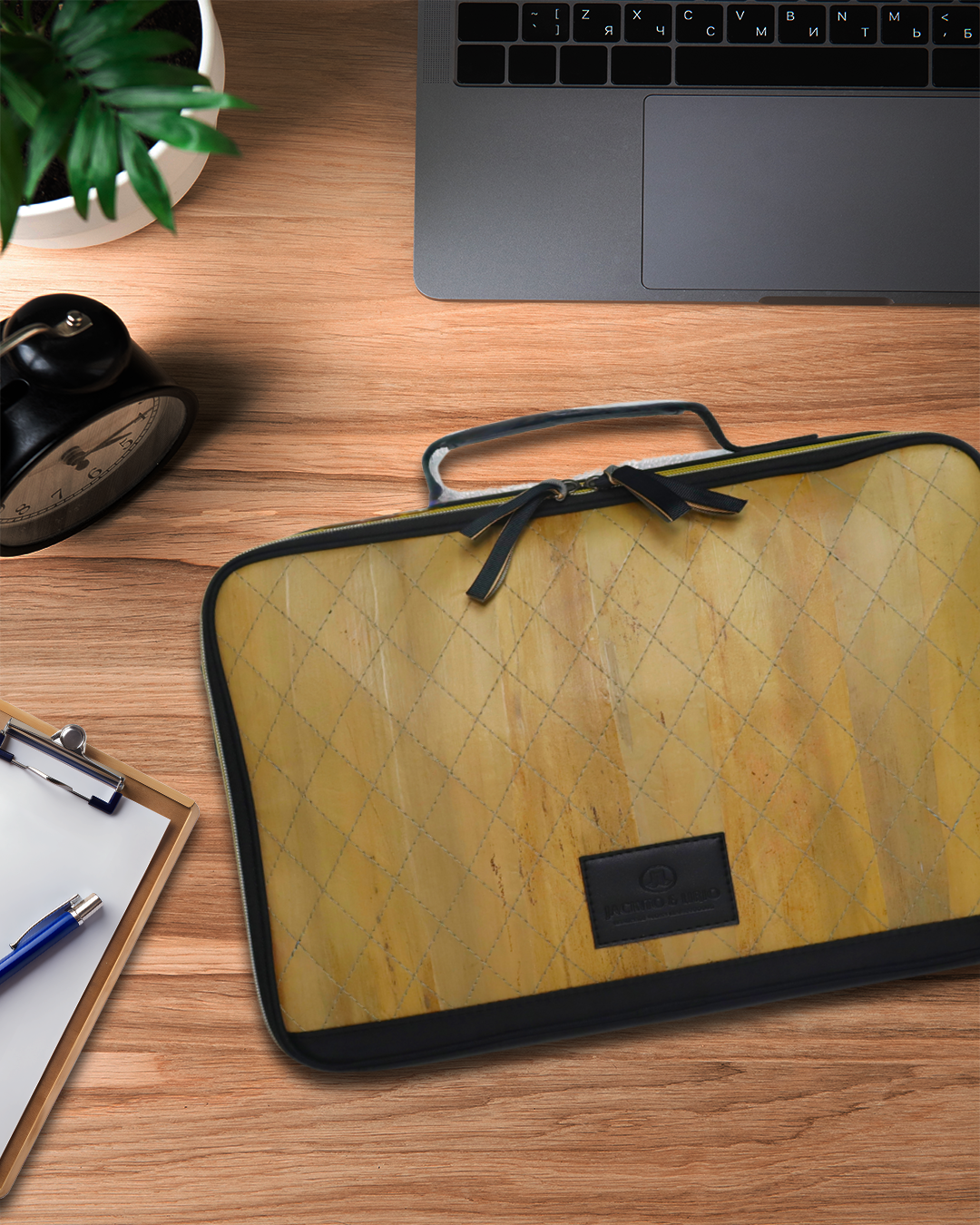 Hiraya bag on a wooden desk with a laptop and plant in the background.