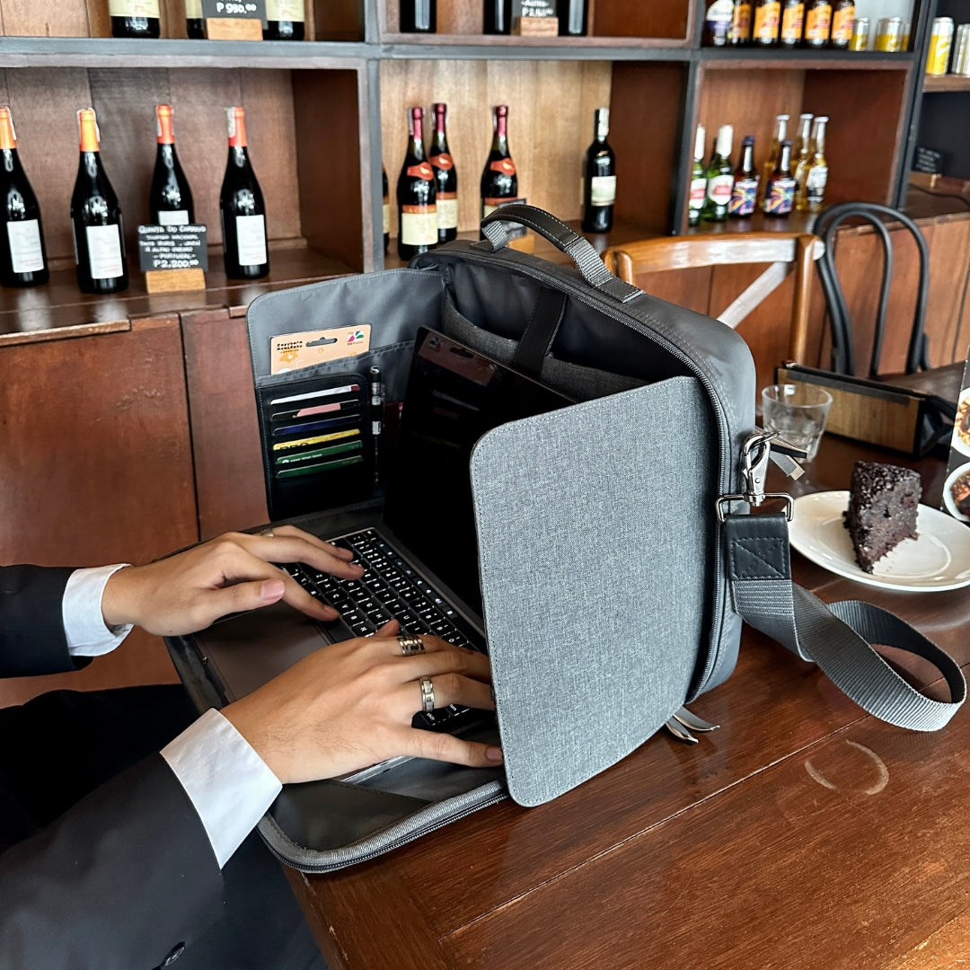 Businessman using a laptop in a Hiraya bag at a bar counter with bottles and a cake in the background.