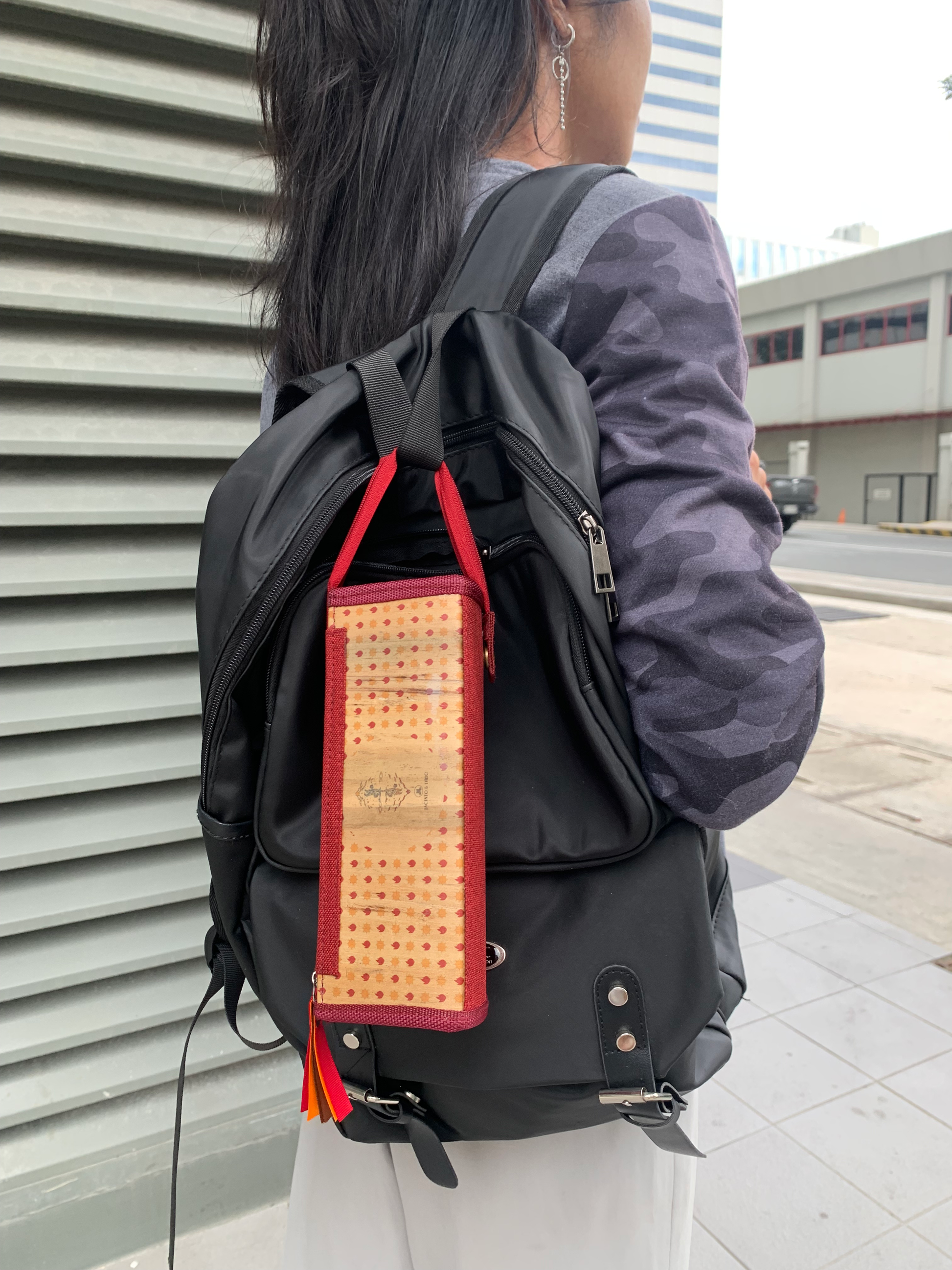 A woman carrying a black backpack that has a vegan leather pencil case with a red polka dot pattern and red fabric hem attached to it. 