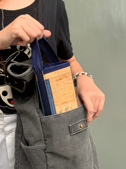 A woman tucking away a vegan leather pencil case with a blue zipper handle into her gray bag.