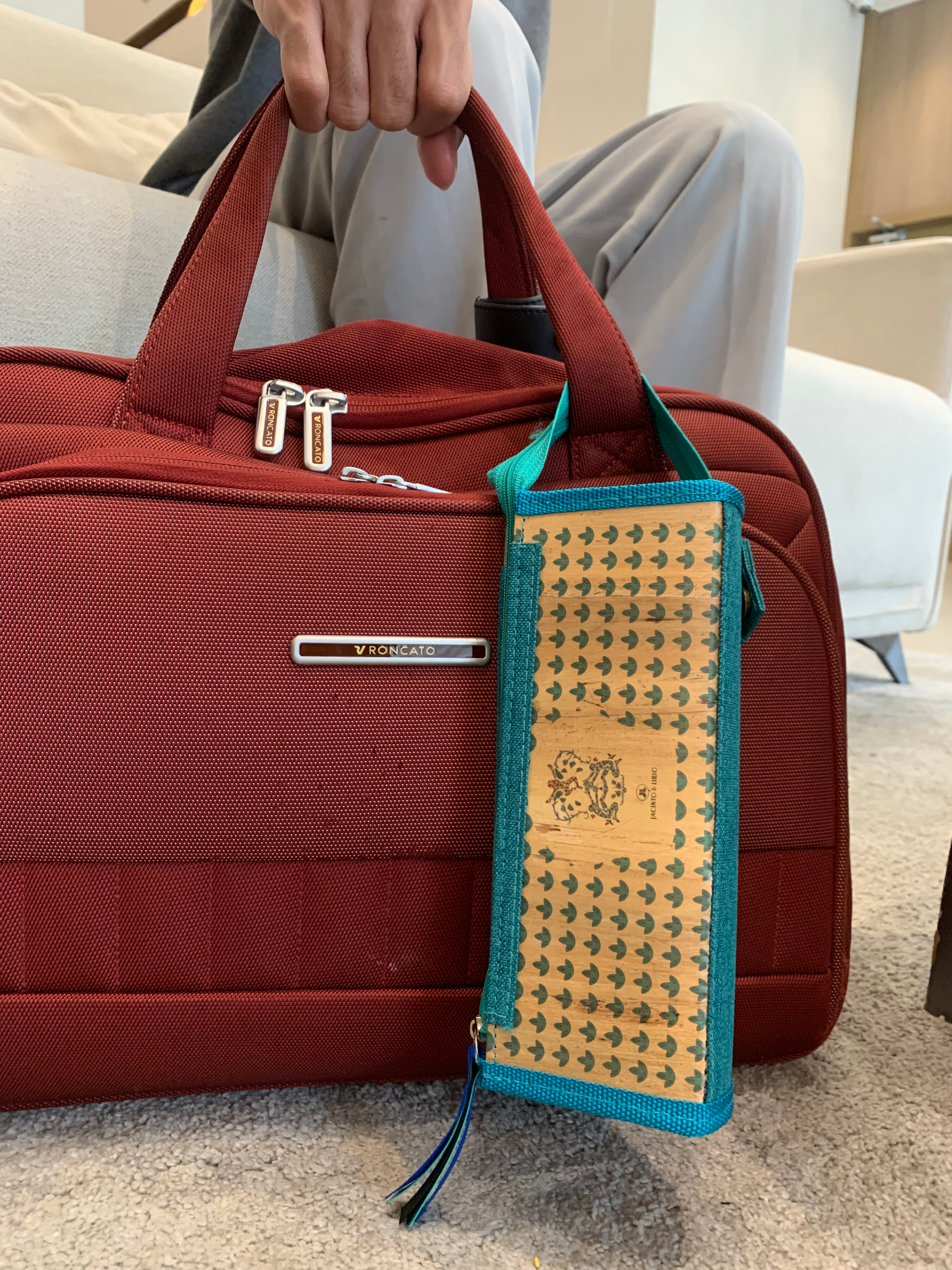 A stylish teal blue vegan leather clutch attached to a red bag's handle.