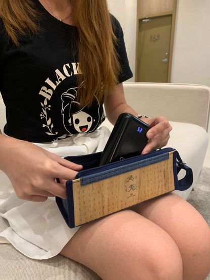 A woman wearing a black shirt with a white skirt tucking away a black powerbank into a vegan leather rectangular clutch with a blue denim hem.