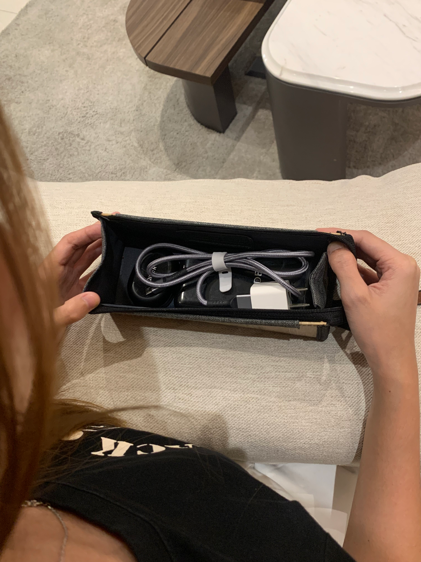 A behind-the-shoulder shot of a woman staring down at a vegan leather pouch that holds her white charger cord and black powerbank