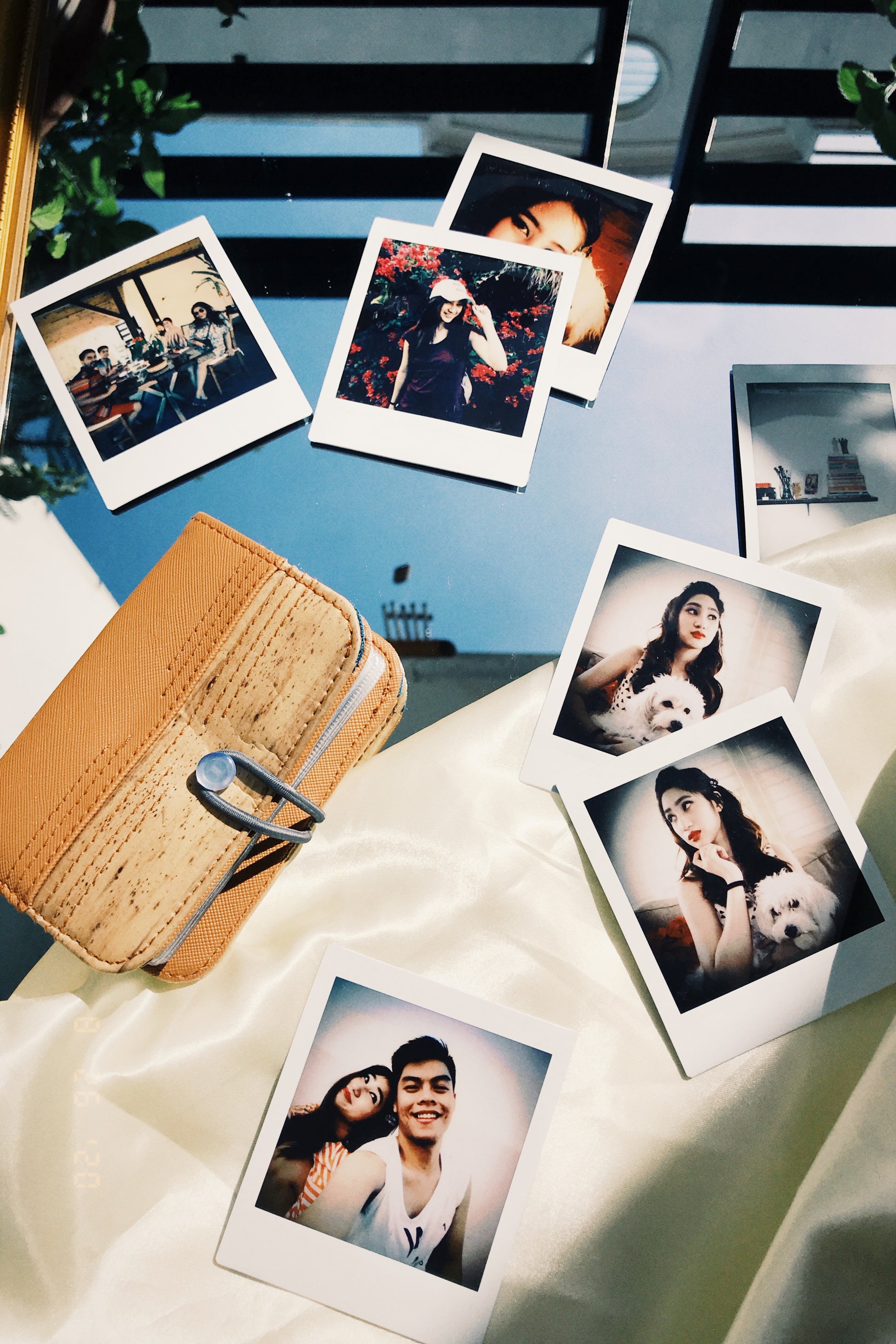 A light brown vegan leather wallet resting on a reflective surface among polaroids of a happy couple.