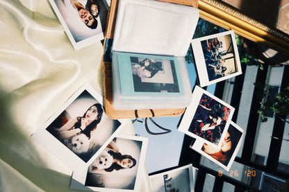 A mini polaroid album laying opened on a surface draped with white silk, alongside other polaroids of a girl and her dog.