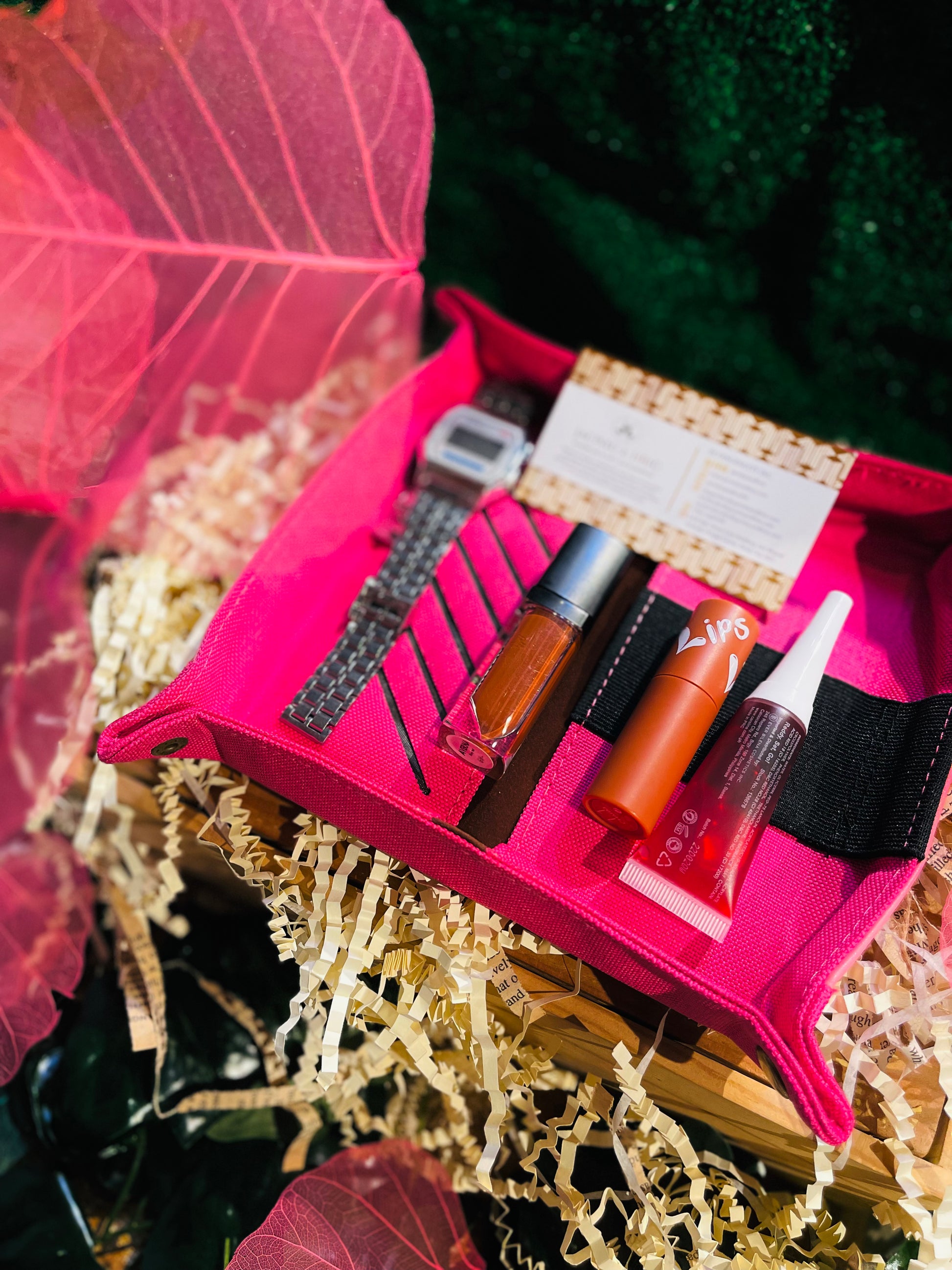 Hot pink leather tray containing a sparkly silver watch and some lip glosses.