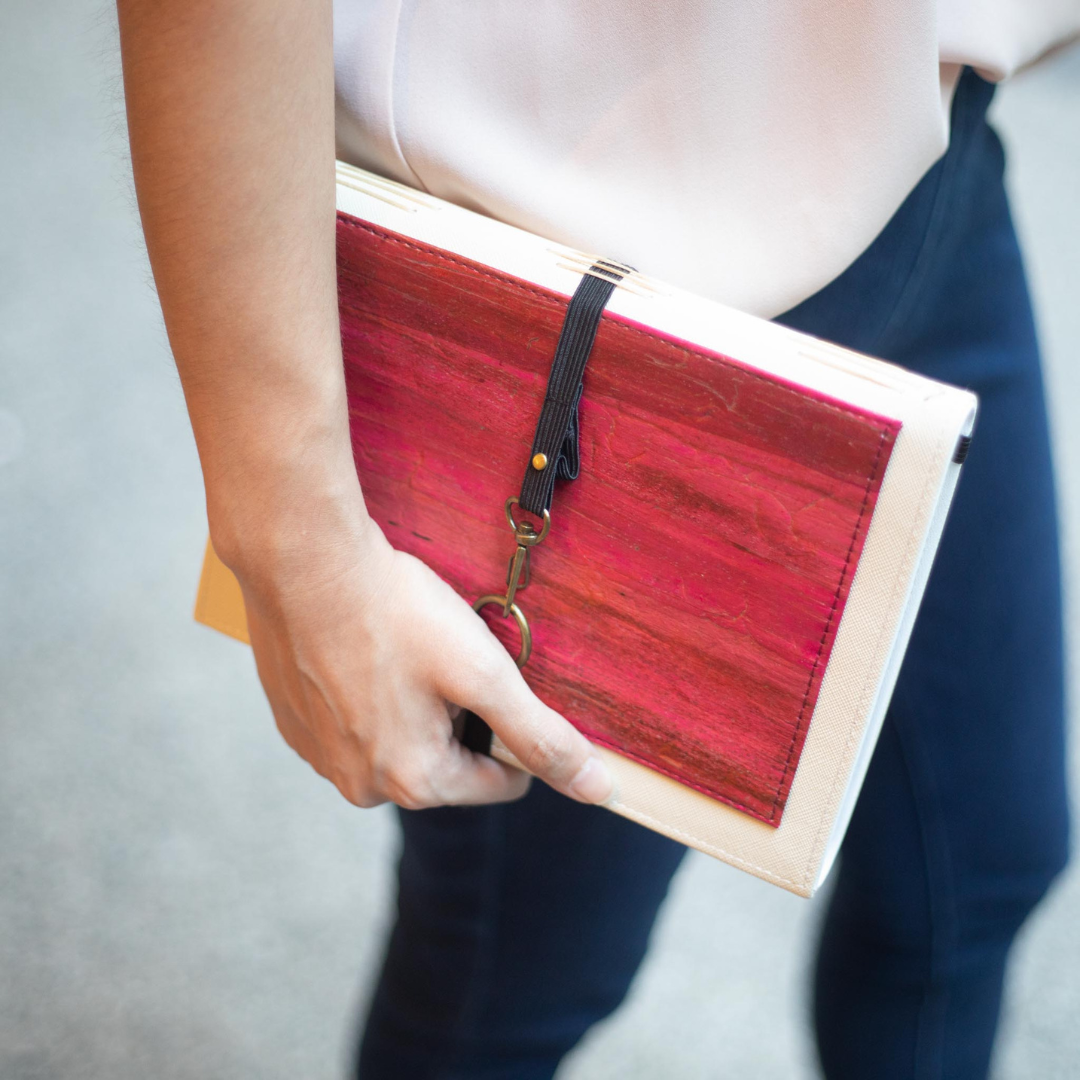 A red and white vegan leather journal with a black strap.