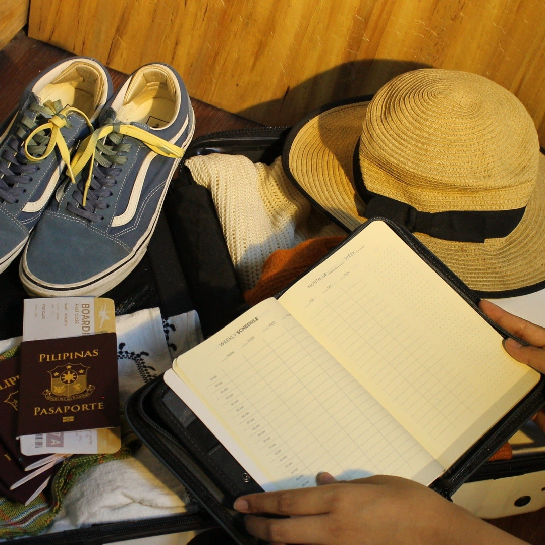 Open suitcase with shoes, a hat, a passport, and Gala, showcasing the weekly planner.