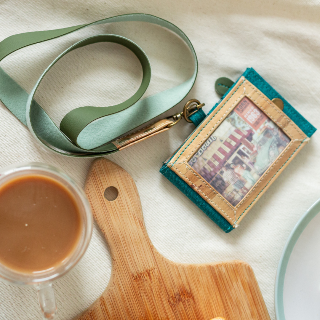 A teal leather lanyard and ID holder next to a cup of coffee