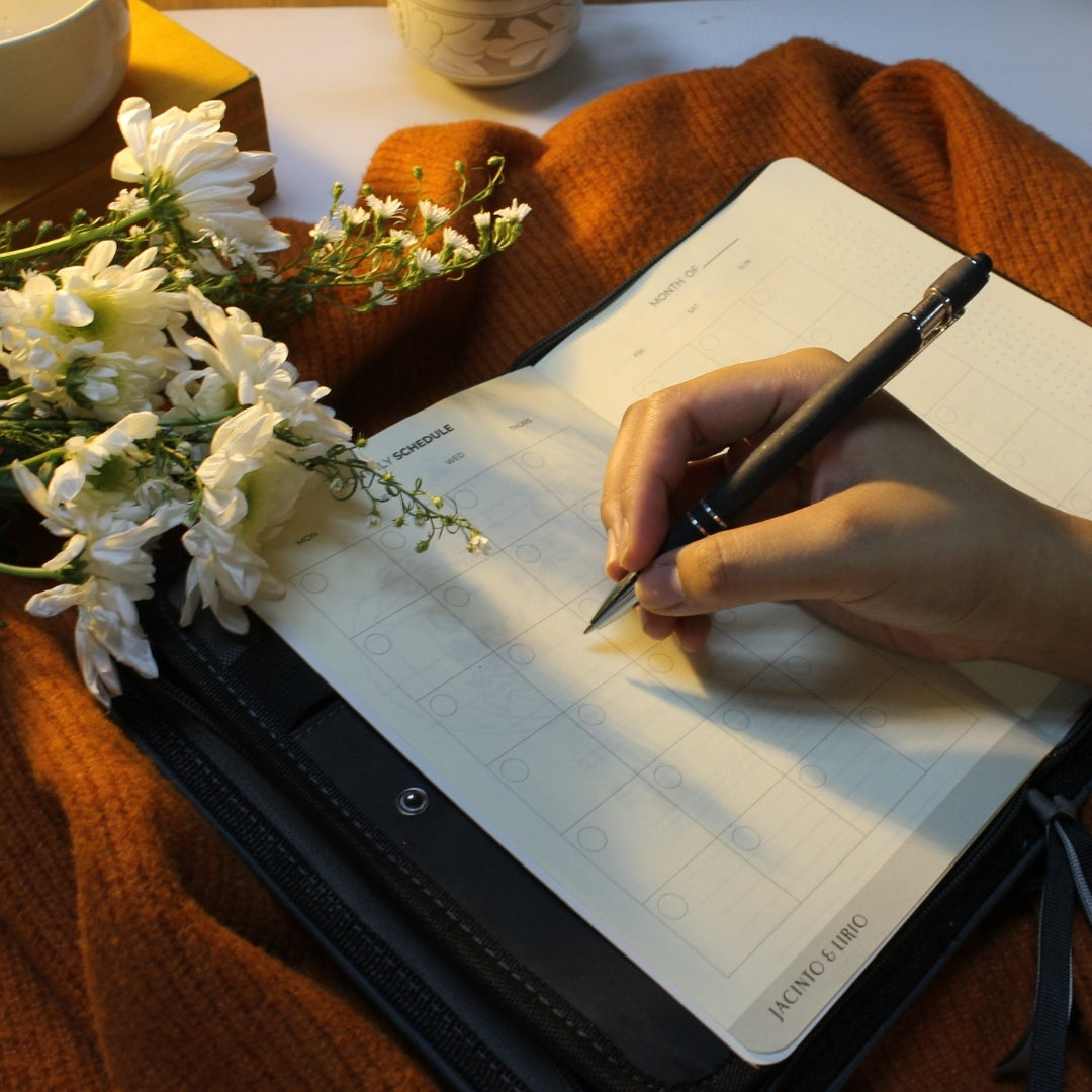 Person writing in the Gala monthly planner with flowers and a cup in the background
