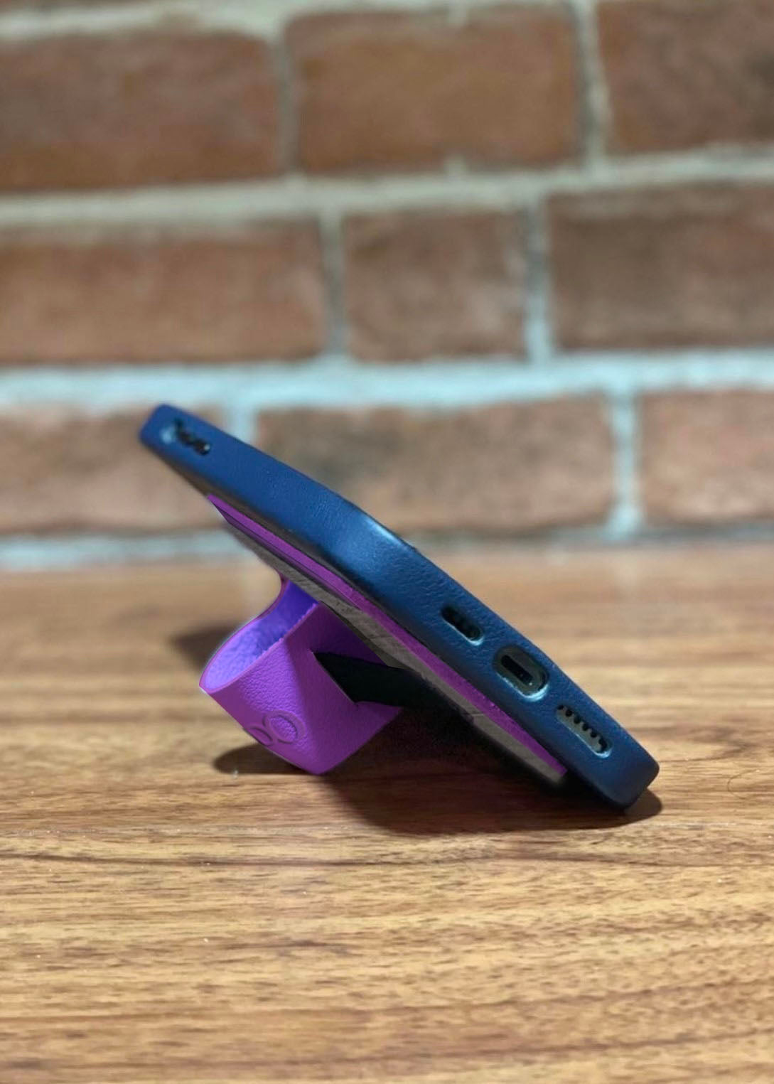 A side view of a purple vegan leather cellphone grip being used as a phone stand by folding the leather in on itself.