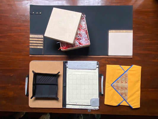 A bundle of vegan leather items perfect for an office employee, such as a deskmat with inlaid pockets, a wrappable laptop case, a catchall tray, and a planner with a corkboard.