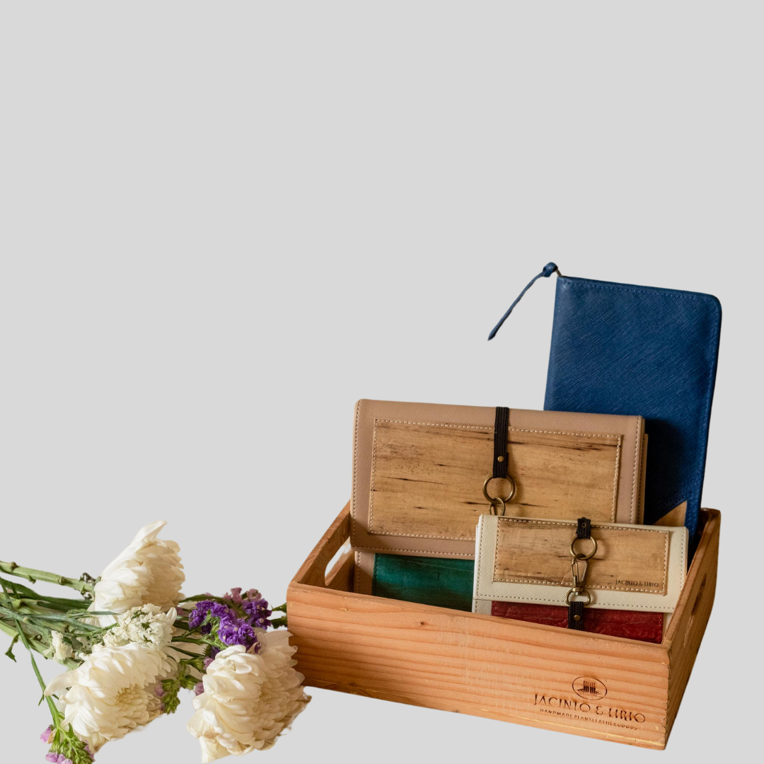 three vegan leather products inside a wooden crate, next to a small bouquet.  There is a blue notebook + wallet, a medium sized closeable notebook, and a mini sized one.