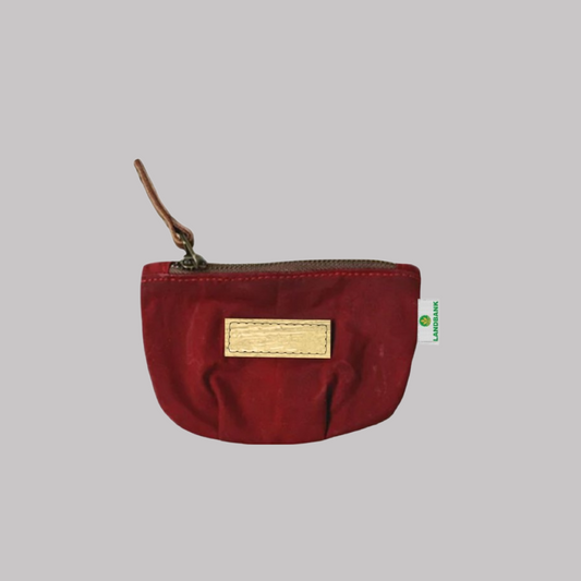 Red coin purse made of waxed canvas and vegan leather, with a zipper and logo plate.